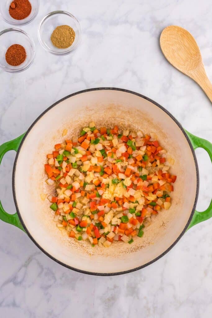 Diced onion, pepper, jalapeno and garlic after softening in a large pot with spices in small bowls nearby on the counter.