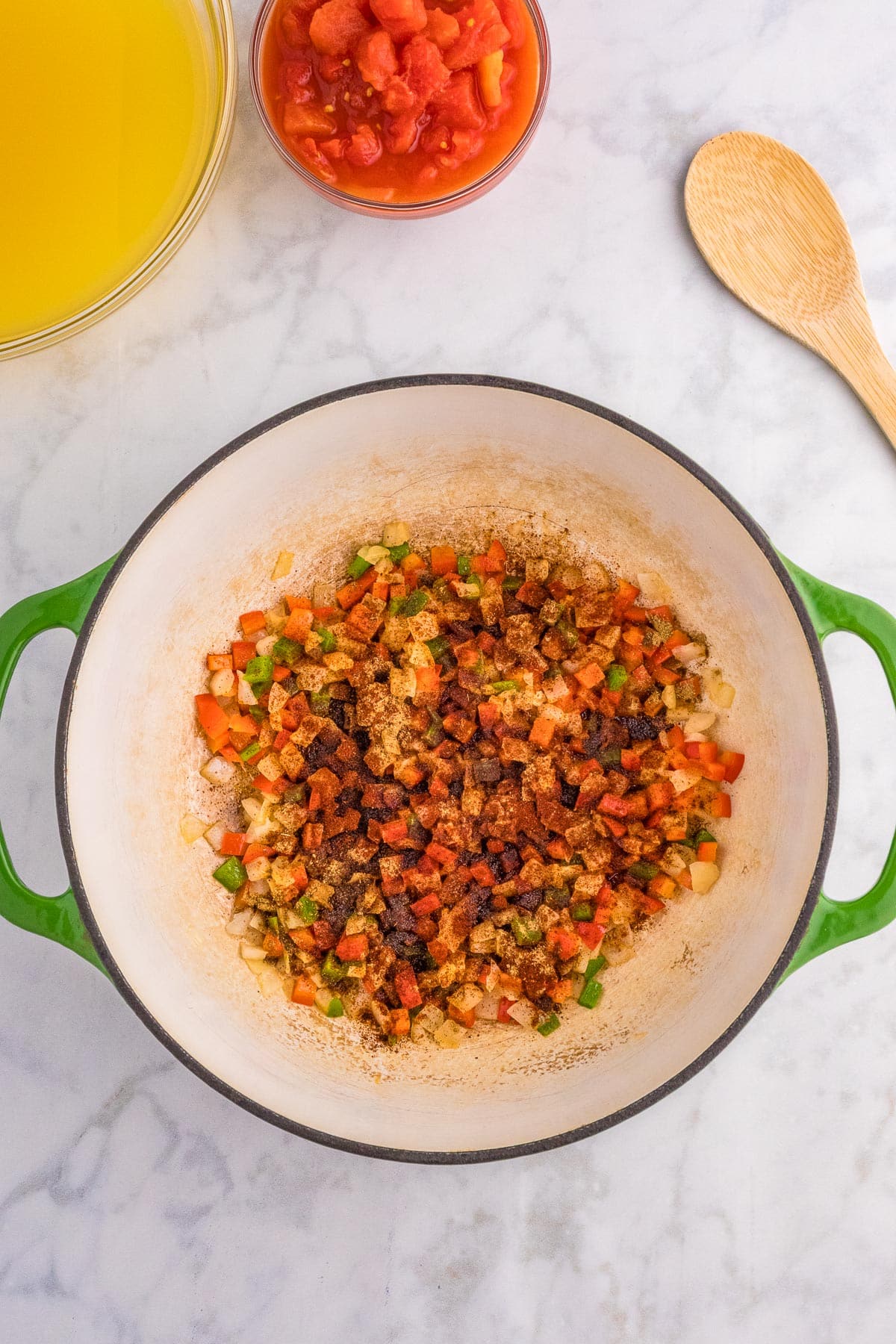 Diced onion, pepper, jalapeno and spices for chicken tortilla soup softening in a large pot with chopped tomatoes in juices and chicken broth in bowls nearby.