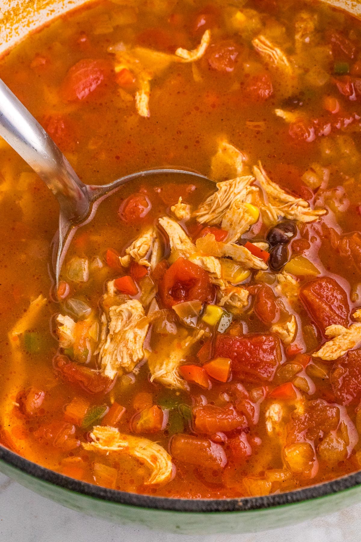 A close-up view of chicken tortilla soup in a large pot being scooped by a ladle.