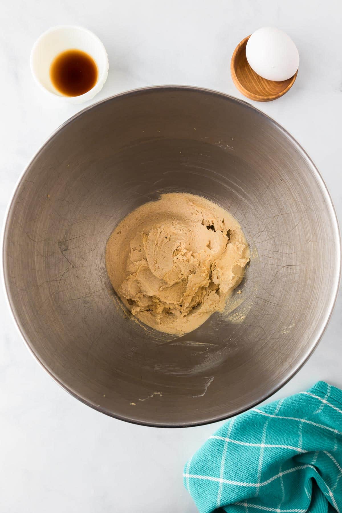 A mixing bowl with creamed butter and sugar with vanilla and an egg nearby for chocolate chip toffee cookies.