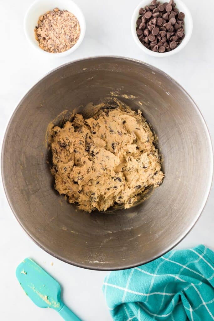 A mixing bowl with cookie dough full of chocolate chips and toffee bits on the counter from above.