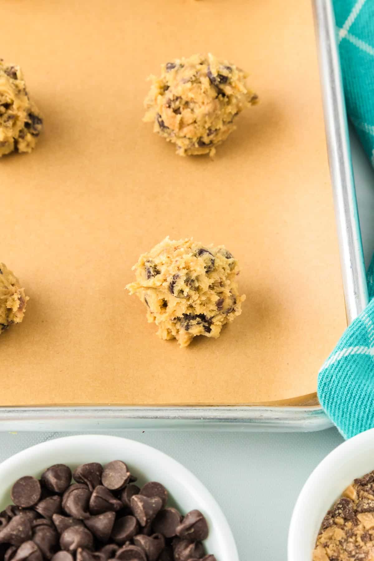 Balls of chocolate chip toffee cookie dough on a parchment-lined baking sheet spaced 2 inches apart.