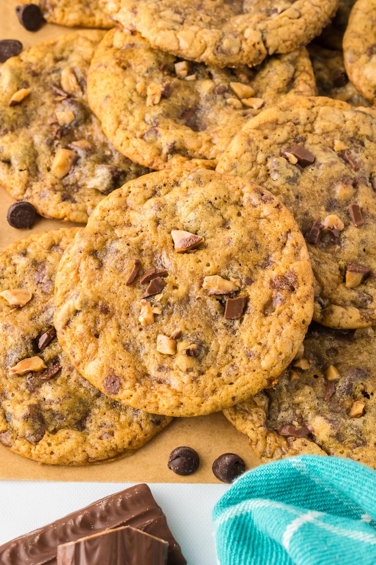 A pile of chocolate chip toffee cookies on parchment paper with a focus on the center cookie.