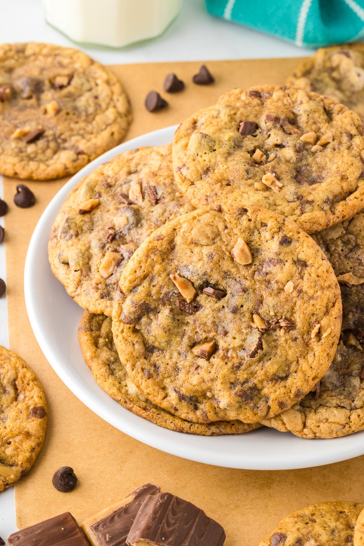 A white plate stacked high with chocolate chip toffee cookies.