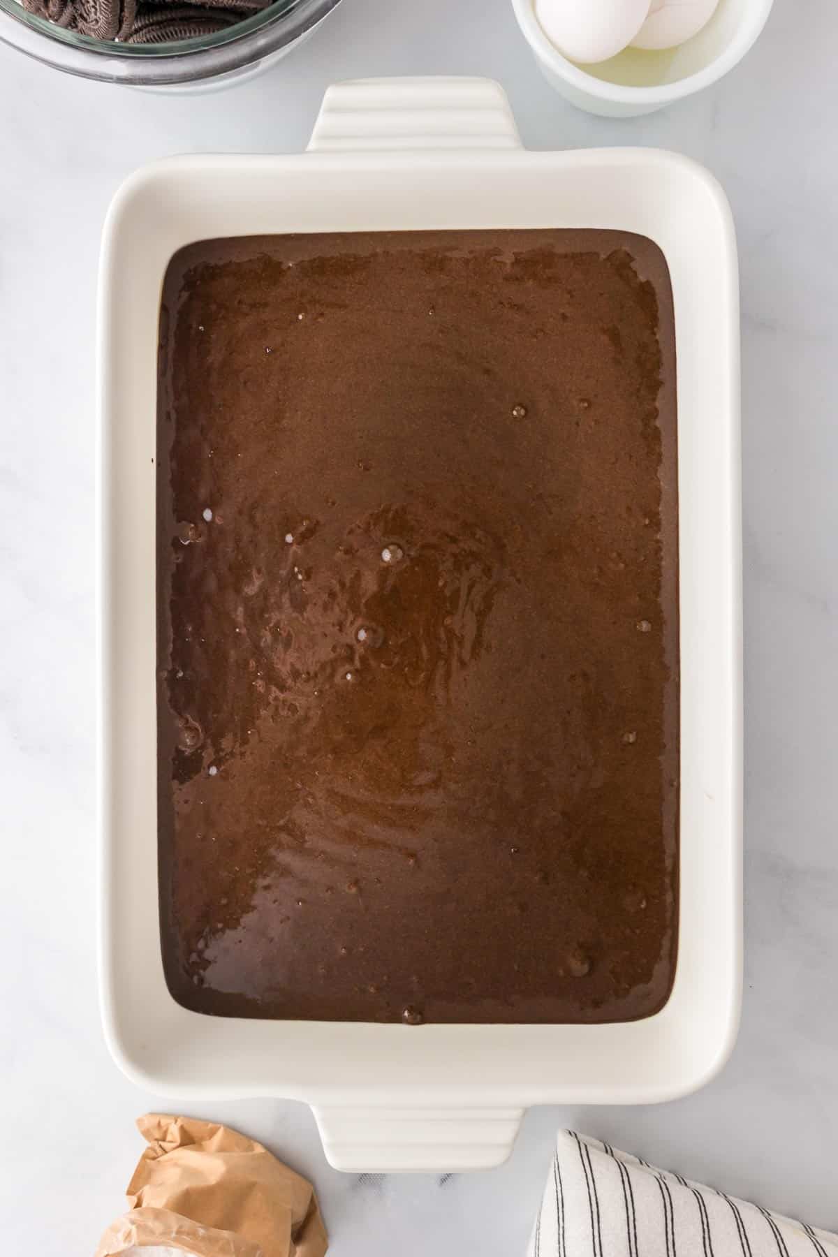 A white baking dish filled with chocolate cake batter before baking for the Halloween poke cake.