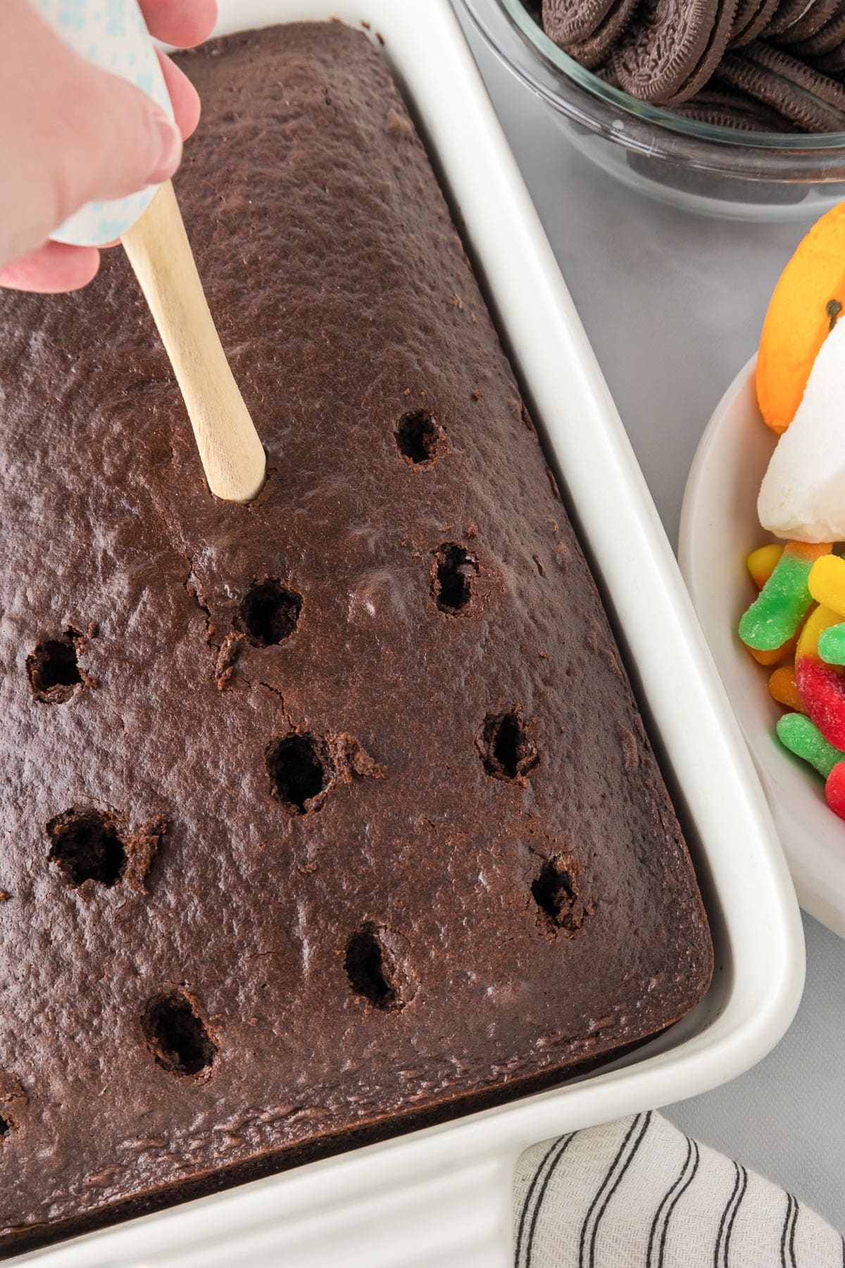 A hand poking holes in a chocolate cake in rows in a rectangular pan for the Halloween poke cake.