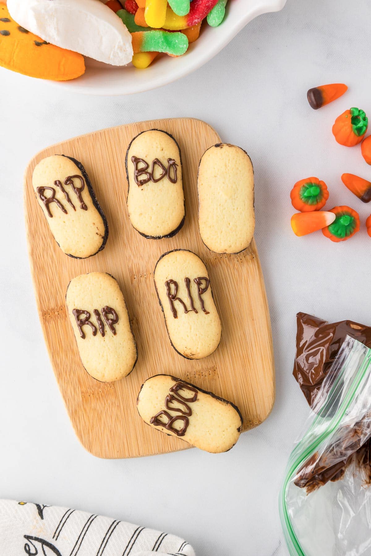 Oval shaped cookies being decorated with chocolate to look like tombstones that read RIP and Boo for Halloween.