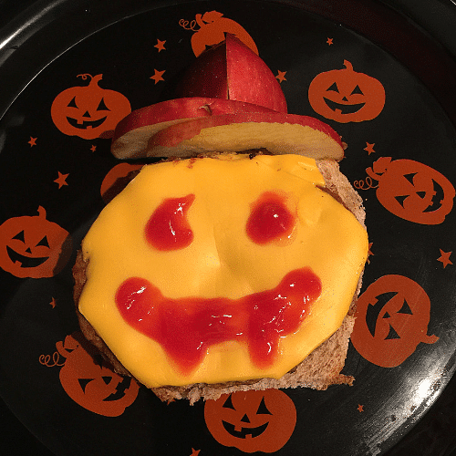 An open face turkey burger covered in cheese with a jack o'lantern face drawn in ketchup.