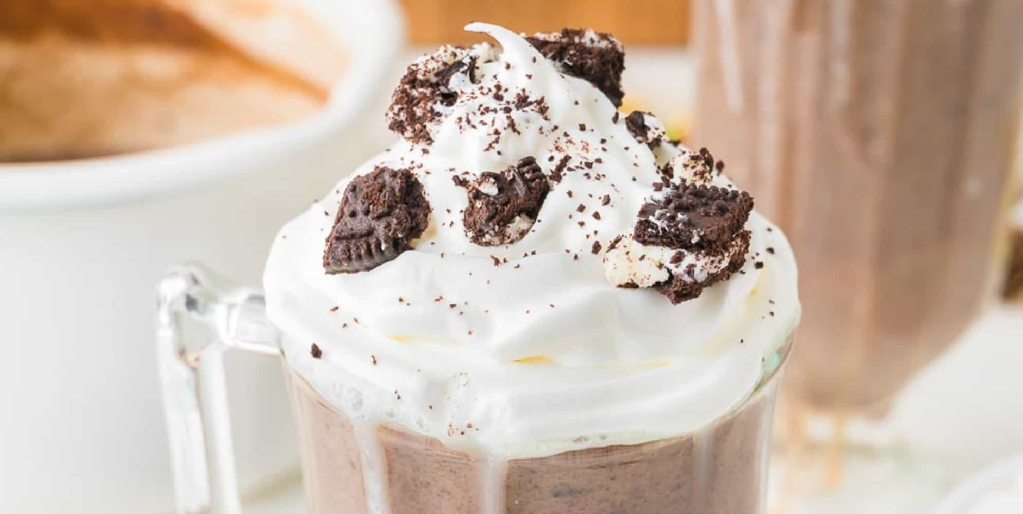 A glass mug filled with Oreo hot chocolate topped with whipped cream and crumbled cookies.