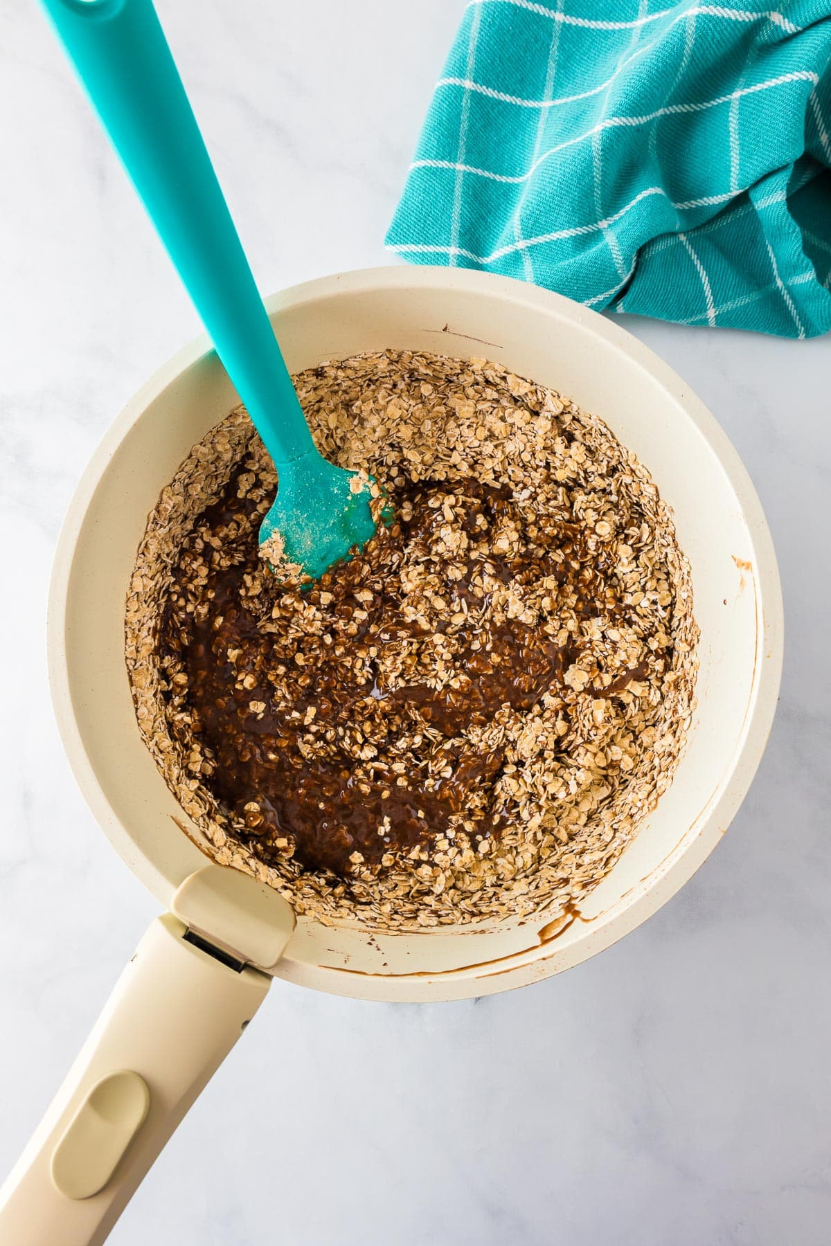 A saucepan containing a mixture of oats and a chocolate peanut butter mixture being mixed with a silicone spatula.