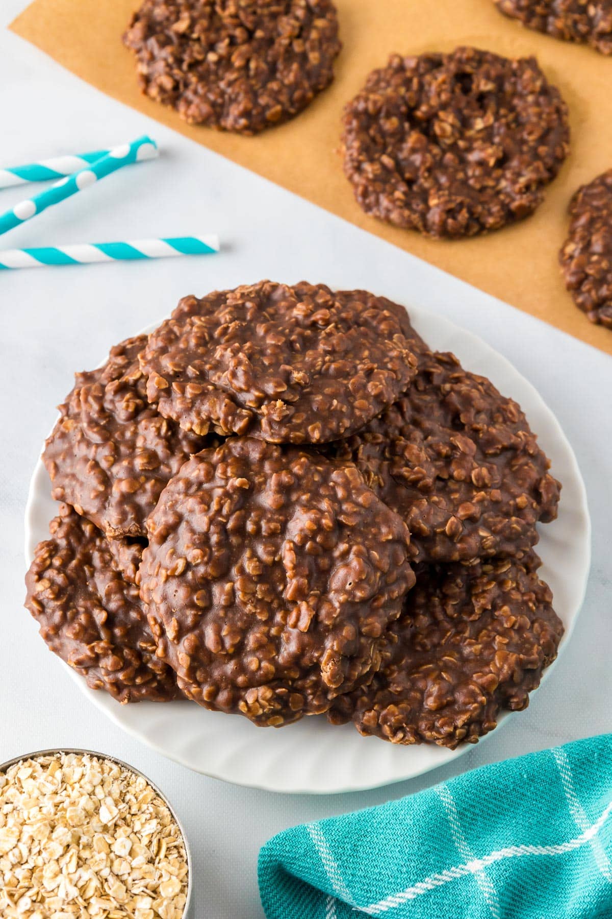 A plate full of no bake chocolate peanut butter cookies with more cooling on parchment paper nearby.