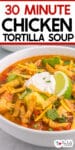 A bowl of chicken tortilla soup garnished with sour cream, avocado slices, lime wedges, crispy tortilla strips, shredded cheese, and chopped cilantro with title text on top of the image.