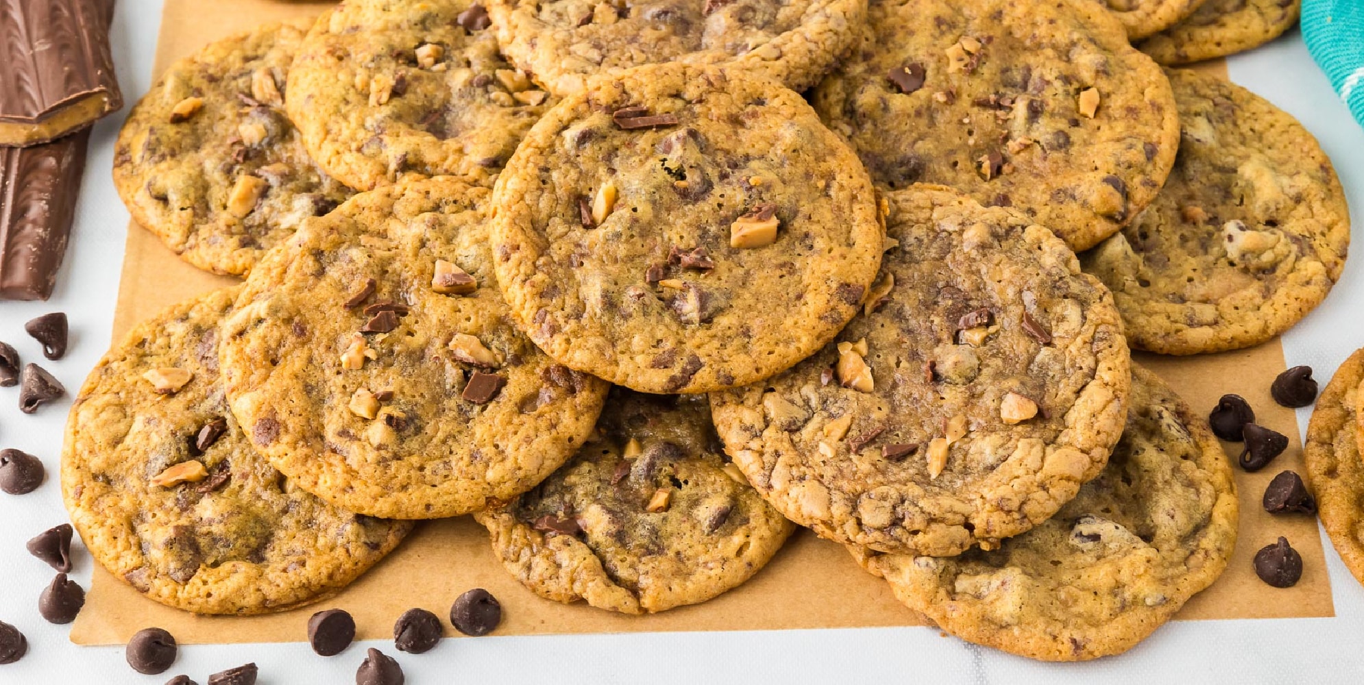 A wide view of a stack of chocolate chip toffee cookies on parchment paper on a counter.