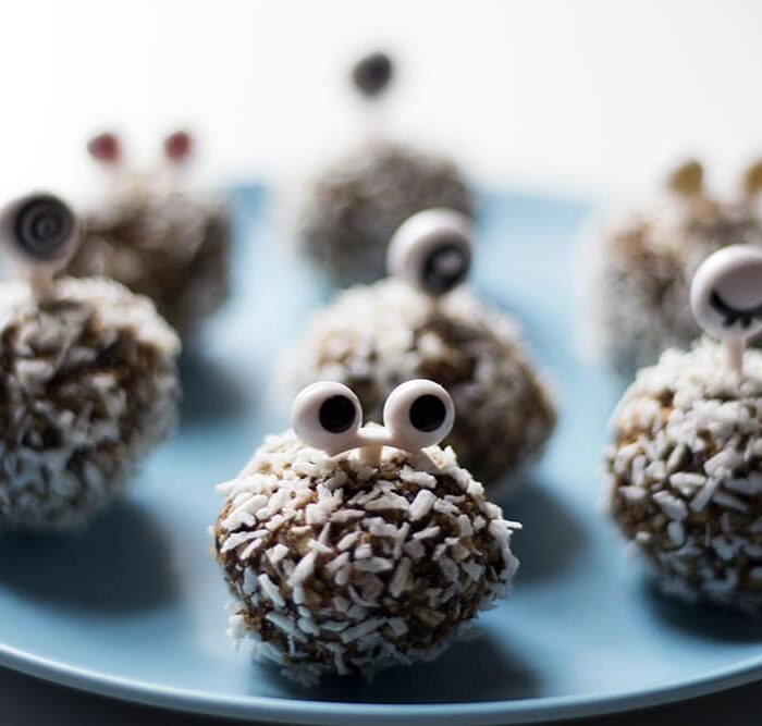 Coconut rolled date energy bites with monster eyes on a plate.