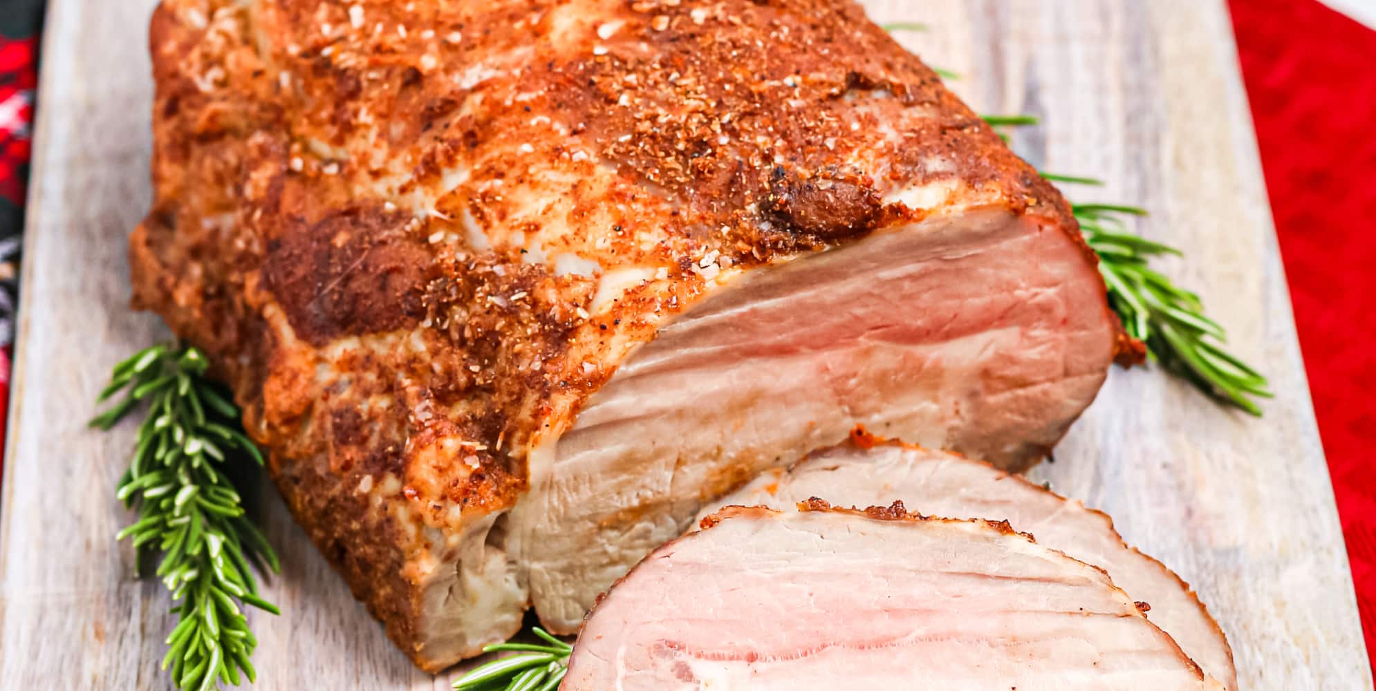 A roasted pork loin sliced with a juicy pink center on a cutting board.