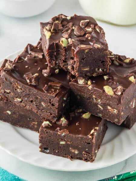 A serving plate with a stack of Andes mint brownies topped with frosting and Andes Mint pieces with the top piece missing a bite.