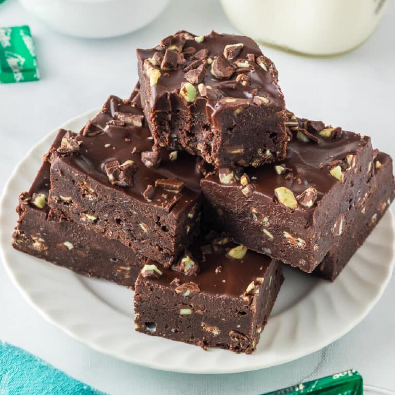 A serving plate with a stack of Andes mint brownies topped with frosting and Andes Mint pieces with the top piece missing a bite.