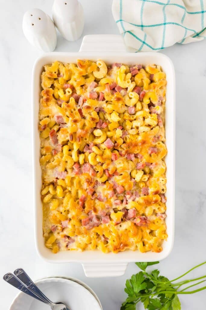 A rectangular baking dish filled with baked cavatappi macaroni and cheese topped with diced ham and baked cheese.