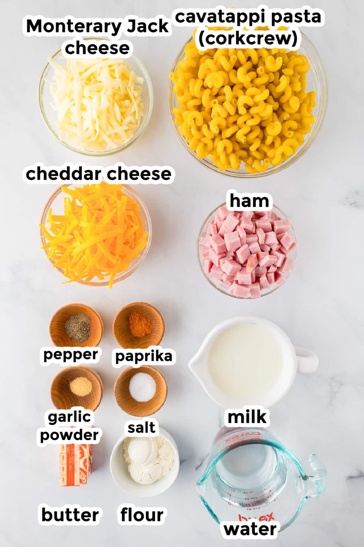 Ingredients for a baked cavatappi mac and cheese with ham recipe in bowls on a counter with text labels,