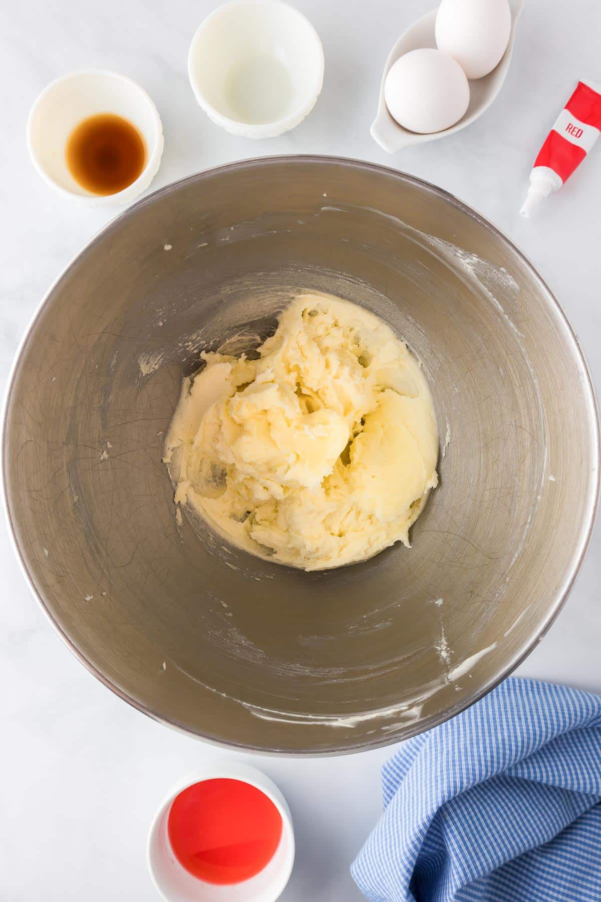 A mixing bowl with butter and sugar creamed together for cherry kiss cookies with more ingredients nearby in bowls