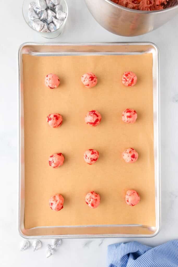 A baking sheet with twelve pink cherry kiss cookie dough balls on a pan.