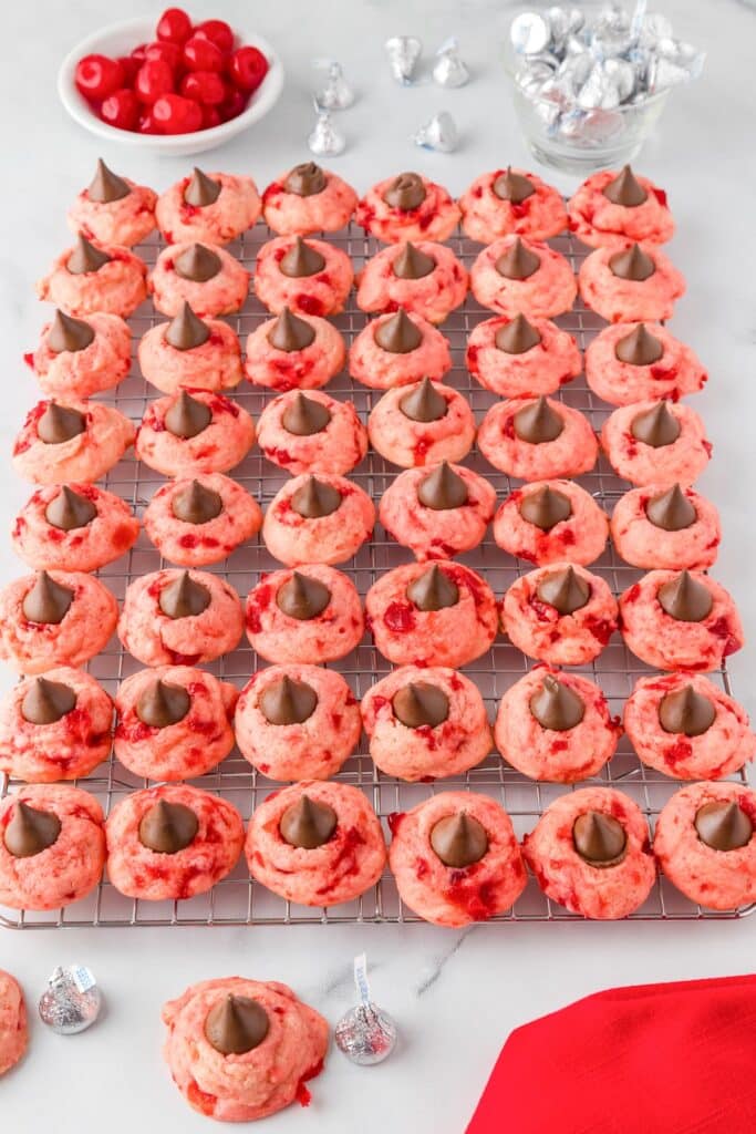 Rows of cherry kiss cookies topped with chocolate candies on a cooling rack.