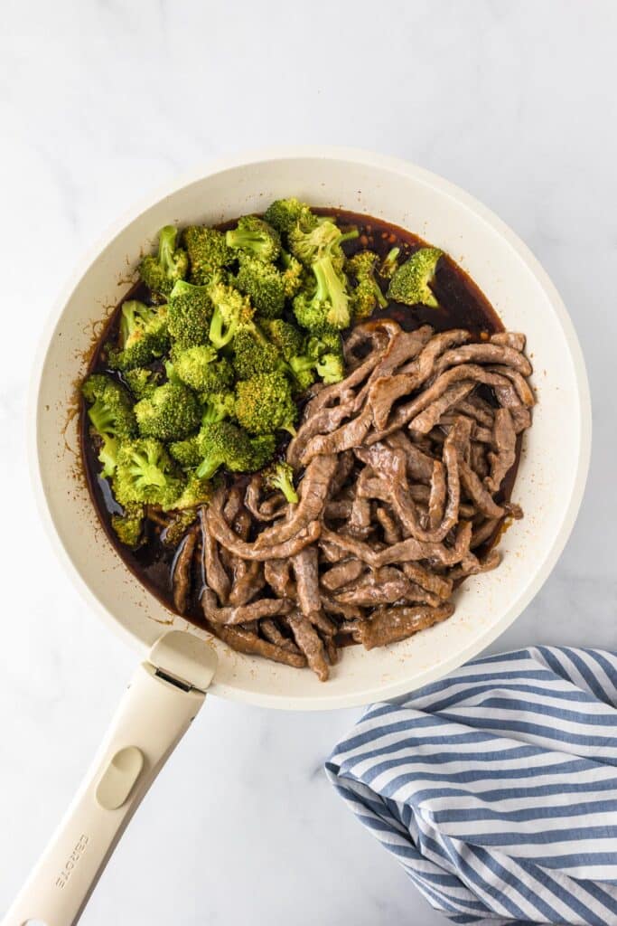 A pan with cooked beef strips and cooked broccoli in a brown sauce for beef and broccoli.