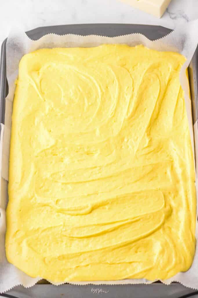 A jelly roll pan lined with parchment paper and filled with raw yellow cake batter spread evenly.