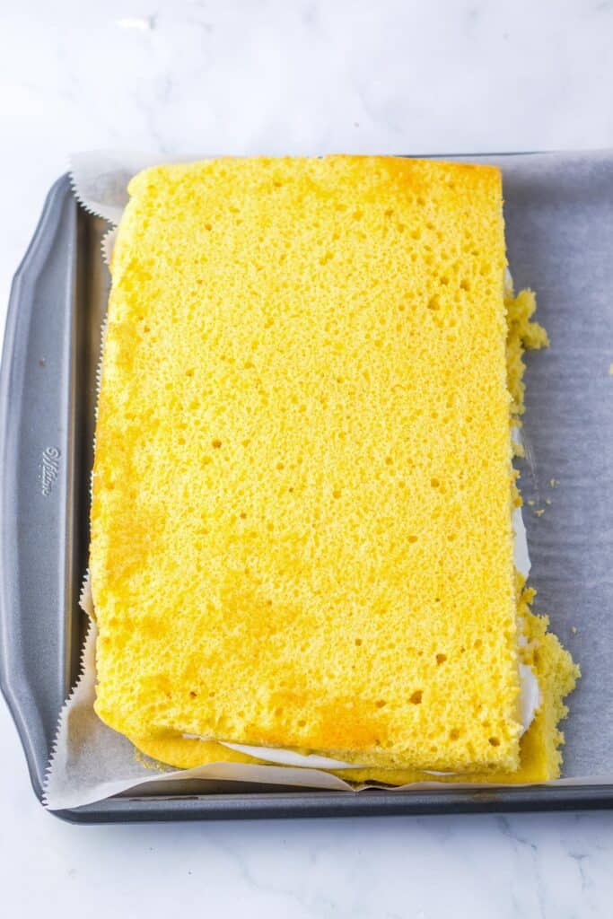 Half of a a rectangular yellowcake rests on a second half of cake with a fluffy marshmallow filling in between filling only half of the pan underneath.