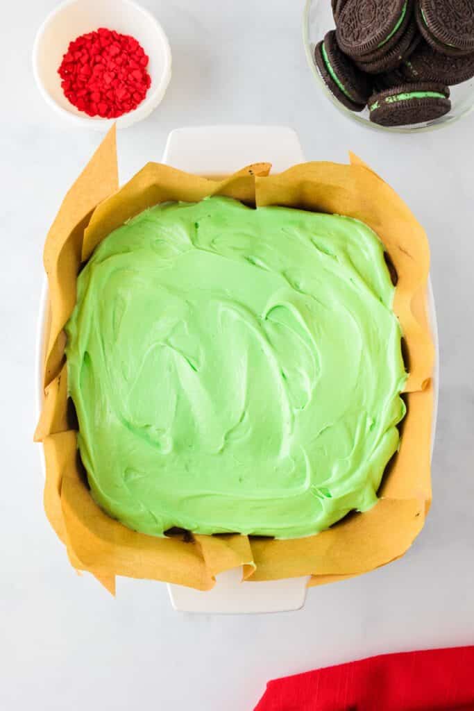 A pan of chocolate Grinch brownies with chunks of mint Oreo cookies after being frosted with green frosting.