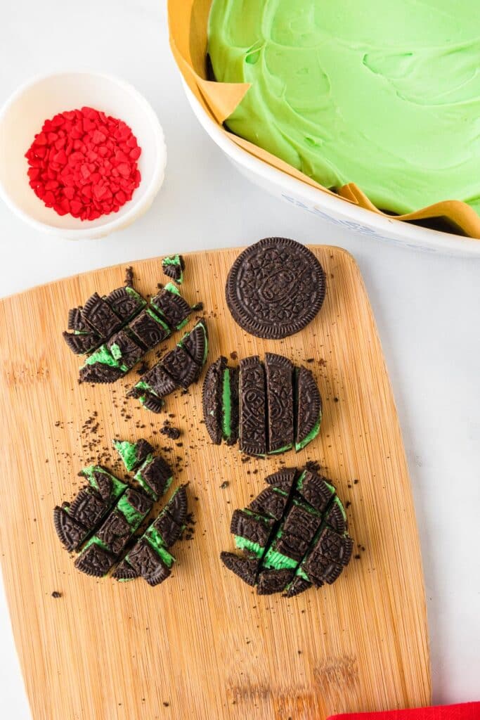 Mint Oreo cookies being roughly chopped for the Grinch brownie topping with frosted brownies in the pan nearby.