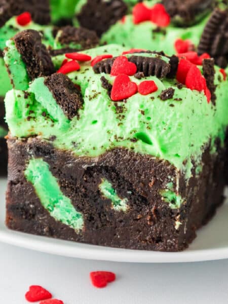 Close-up of a frosted Grinch brownie with mint Oreo pieces and heart sprinkles on a plate.