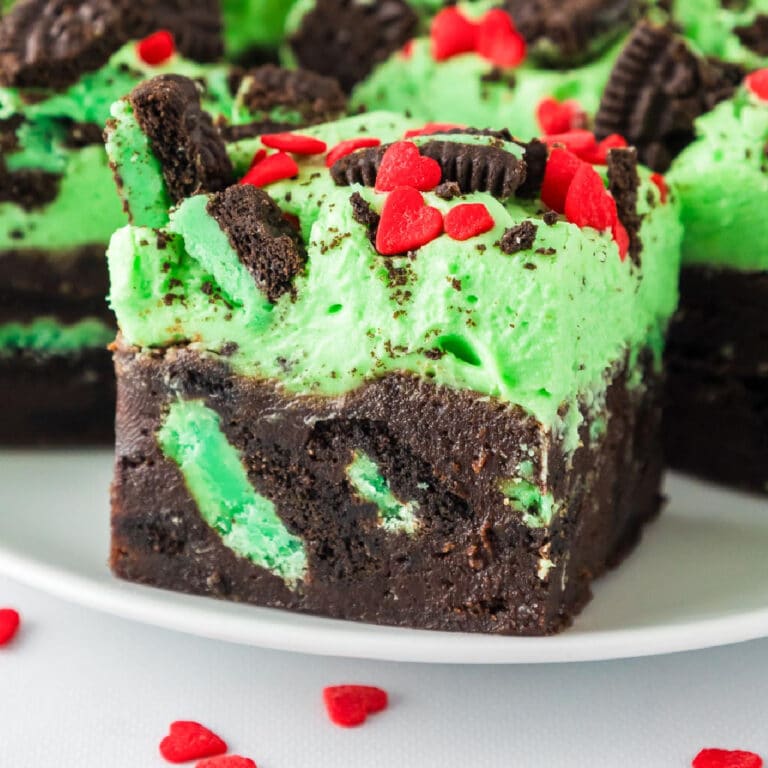 Close-up of a frosted Grinch brownie with mint Oreo pieces and heart sprinkles on a plate.