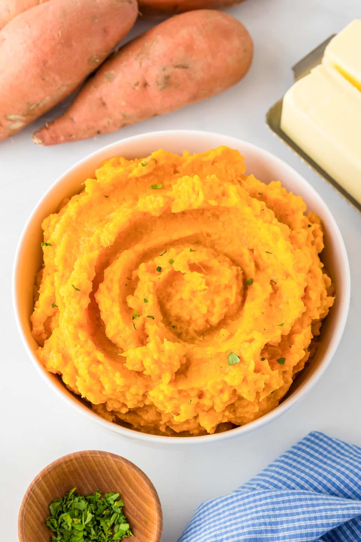 A bowl of mashed sweet potatoes garnished with fresh herbs.