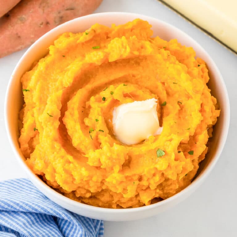 A bowl of maple mashed sweet potatoes in a bowl in a swirl pattern with a pat of melted butter on top on a table.