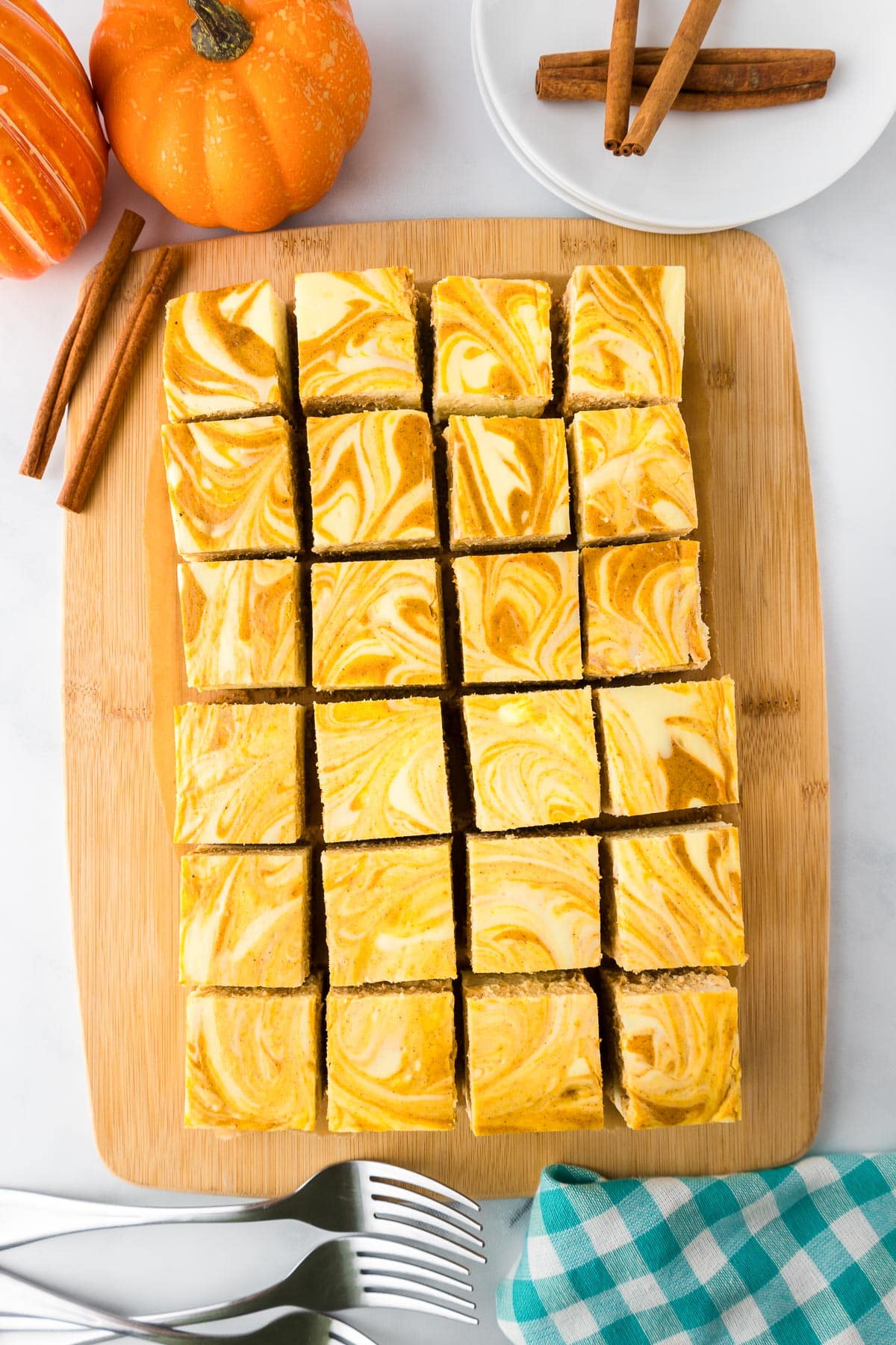 Sliced pumpkin swirl cheesecake bars on a cutting board, surrounded by small pumpkins and cinnamon sticks.