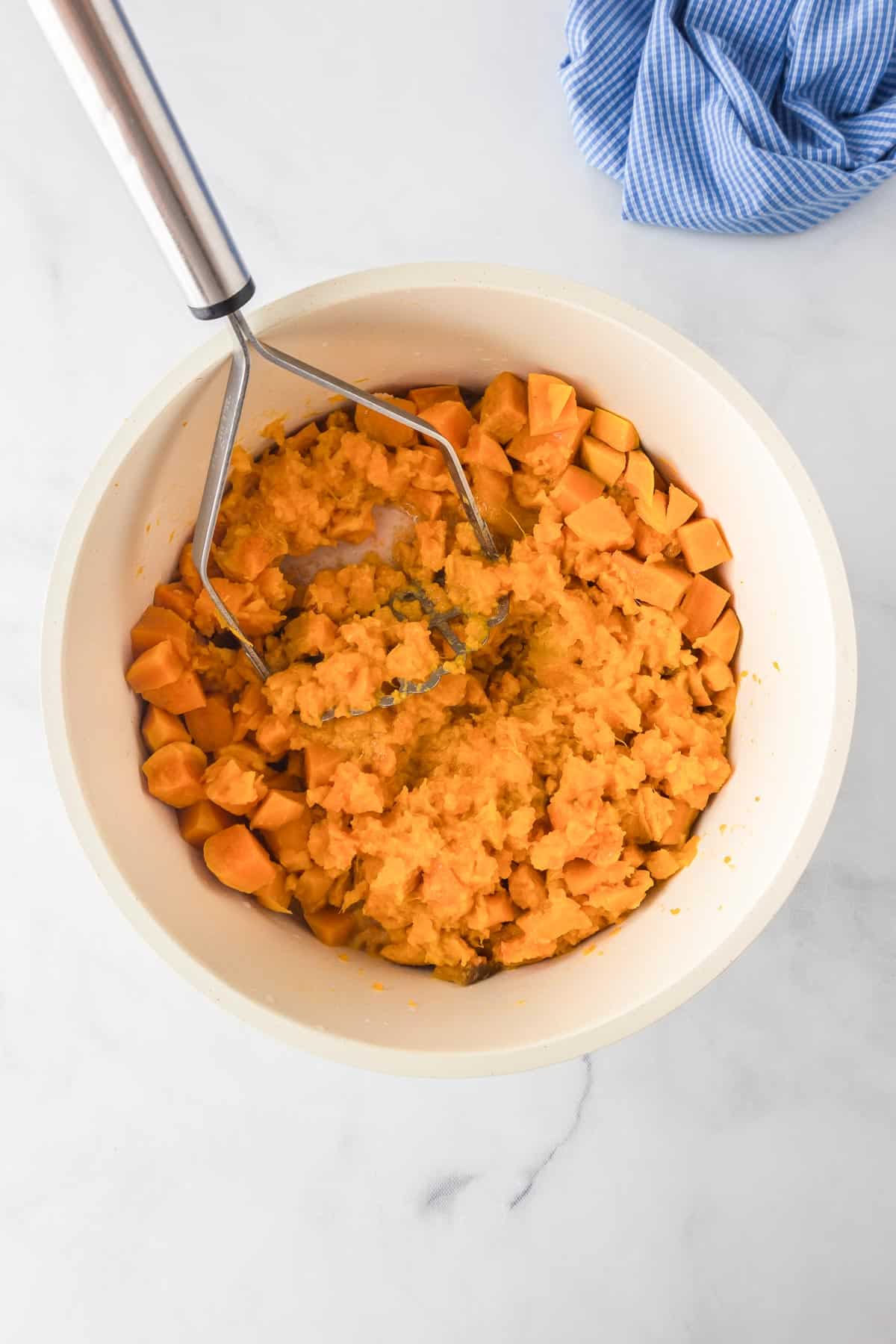 Cooked sweet potatoes in a bowl being mashed with a potato masher.