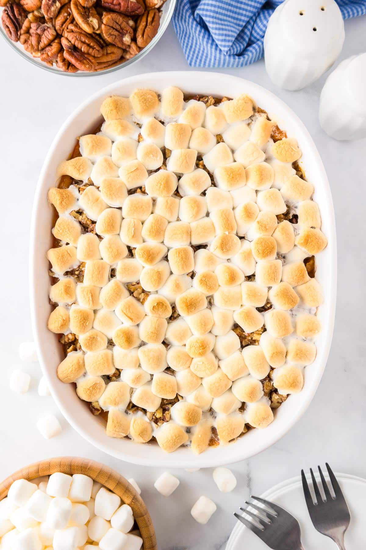 Baked sweet potato casserole topped with toasted marshmallows on a counter with pecans in a bowl nearby.