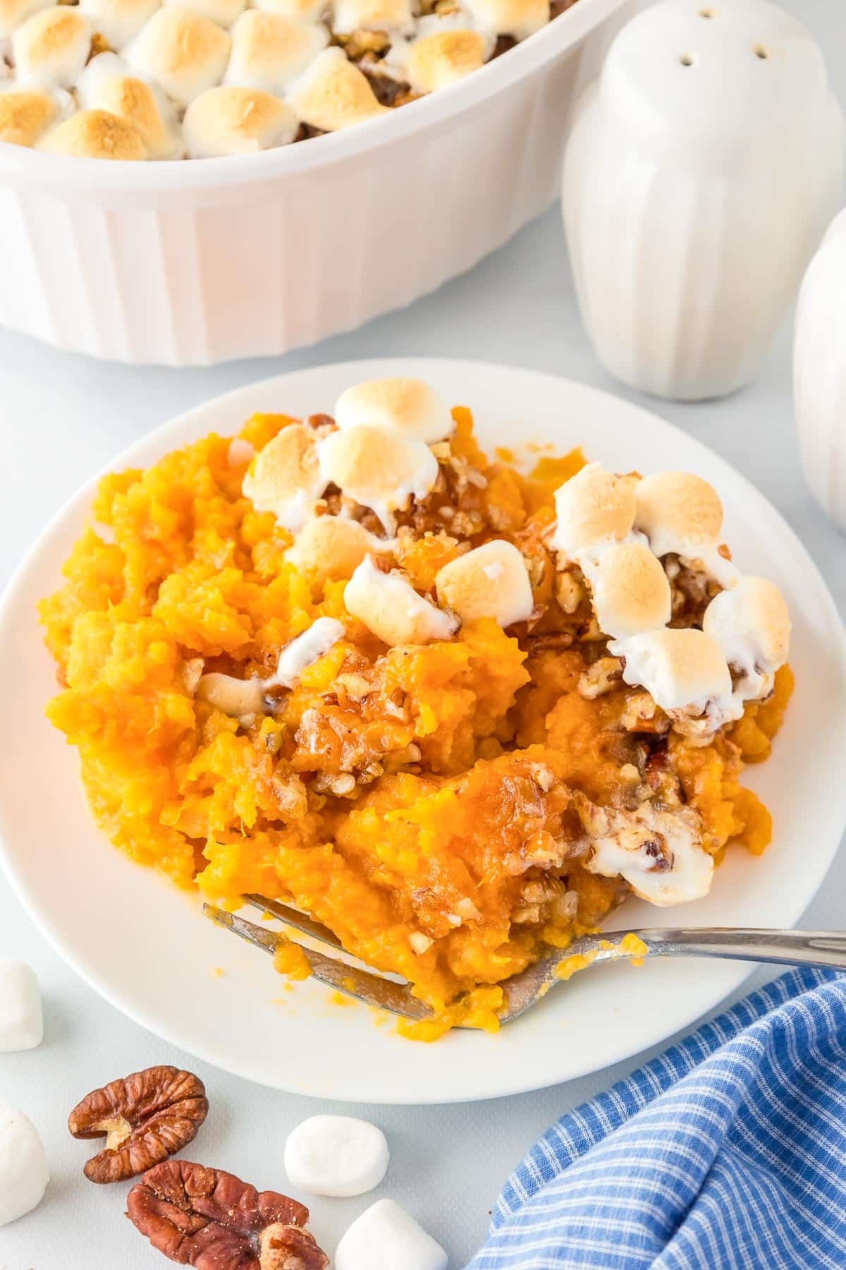 Plate of sweet potato casserole topped with toasted marshmallows, with a fork on the side with a pan of sweet potato casserole in the background.