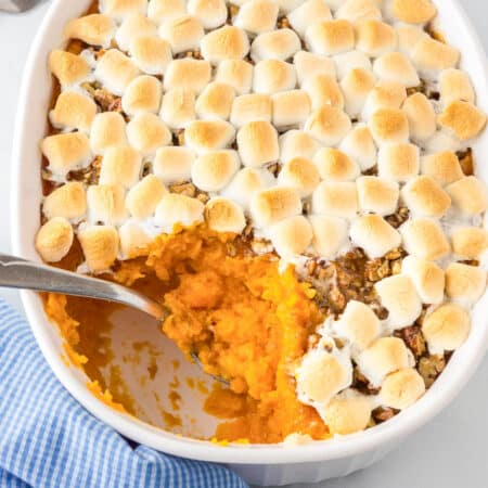 A casserole dish with sweet potato casserole topped with pecans and toasted marshmallows with a spoon scooping a scoop.