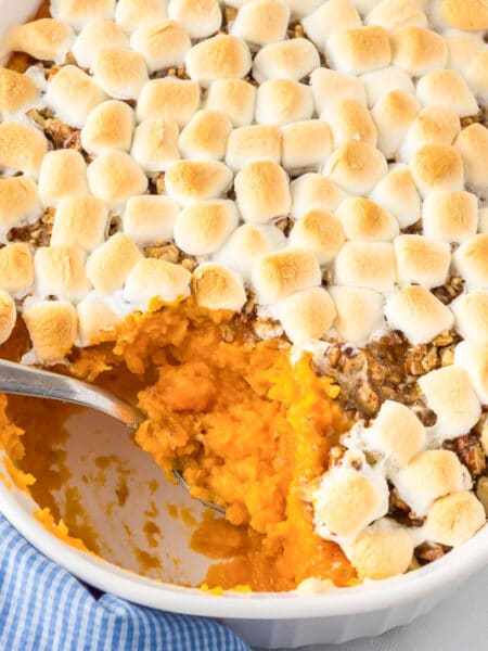 A casserole dish with sweet potato casserole topped with pecans and toasted marshmallows with a spoon scooping a scoop.