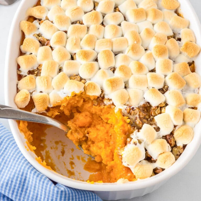 A casserole dish with sweet potato casserole topped with pecans and toasted marshmallows with a spoon scooping a scoop.