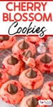 Cherry blossom cookies topped with chocolate kisses on a cooling rack, with one cookie missing a bite and title text across the image.