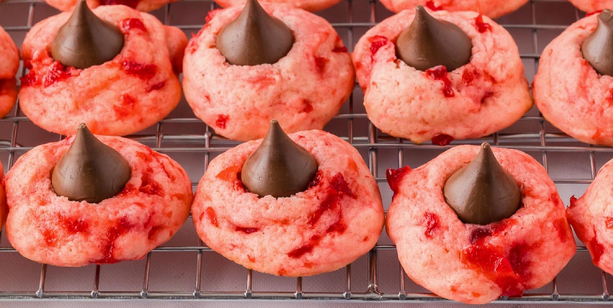 A pink cherry kiss cookie with a chocolate kiss in the center placed on a piece of parchment paper.