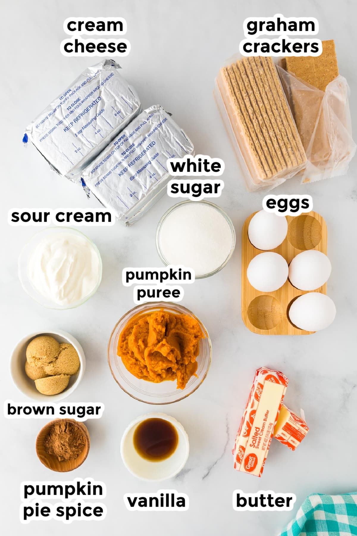 Ingredients for pumpkin swirl cheesecake bars on a counter in bowls with text labels.