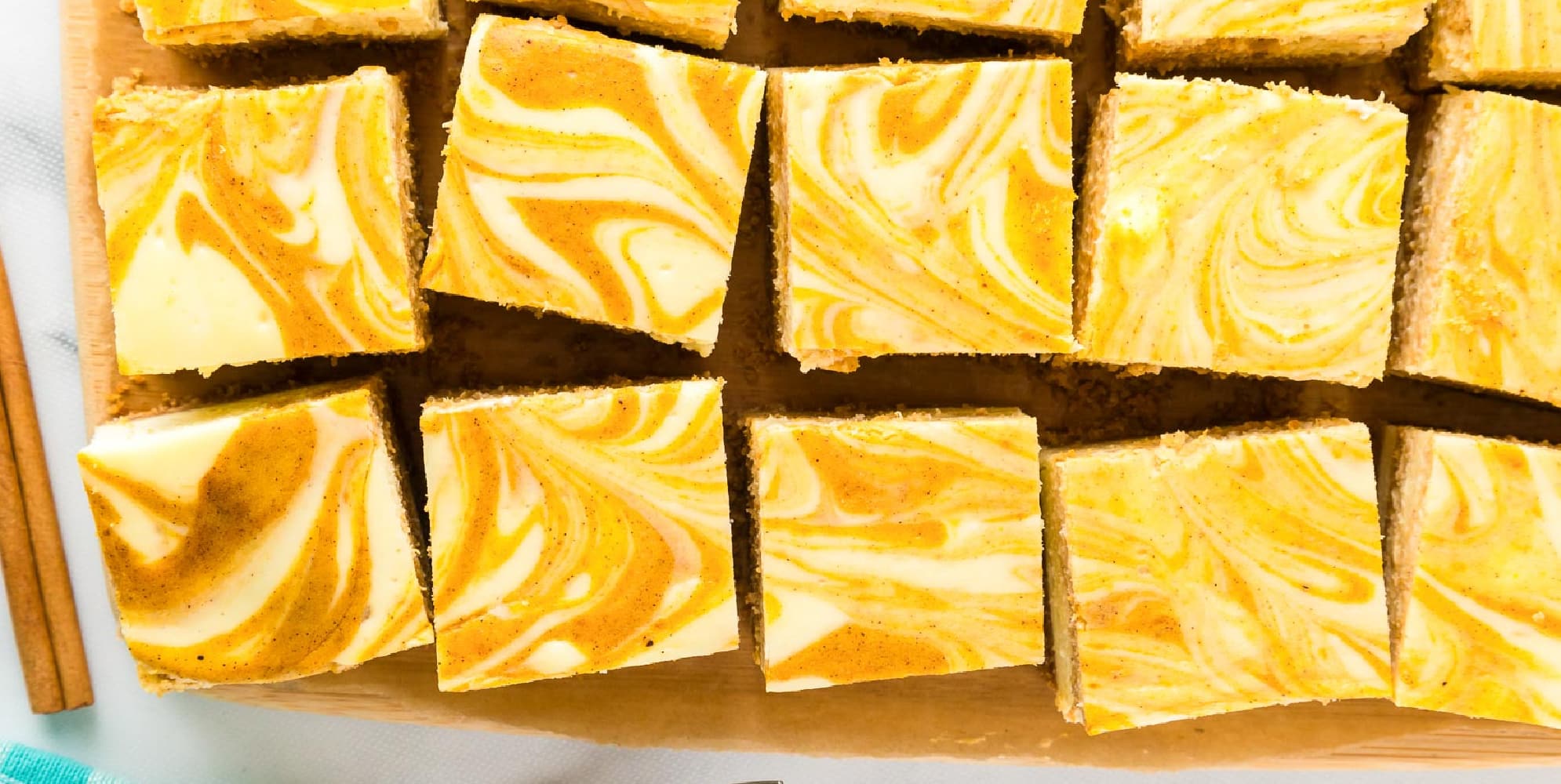 Wide view of sliced pumpkin swirl cheesecake bars from above on a cutting board.