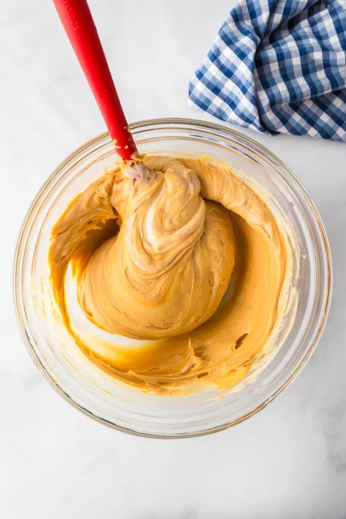 A mixing bowl full of 2 ingredient peanut butter fudge being mixed with a silicone spatula.