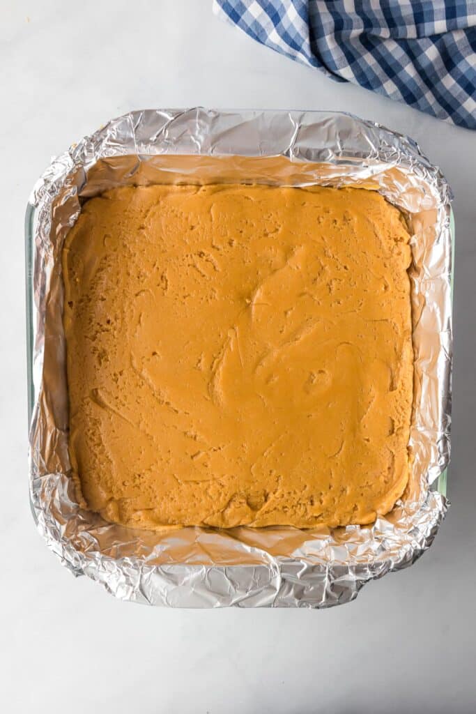 A square baking dish lined with foil full of peanut butter fudge after it has set.