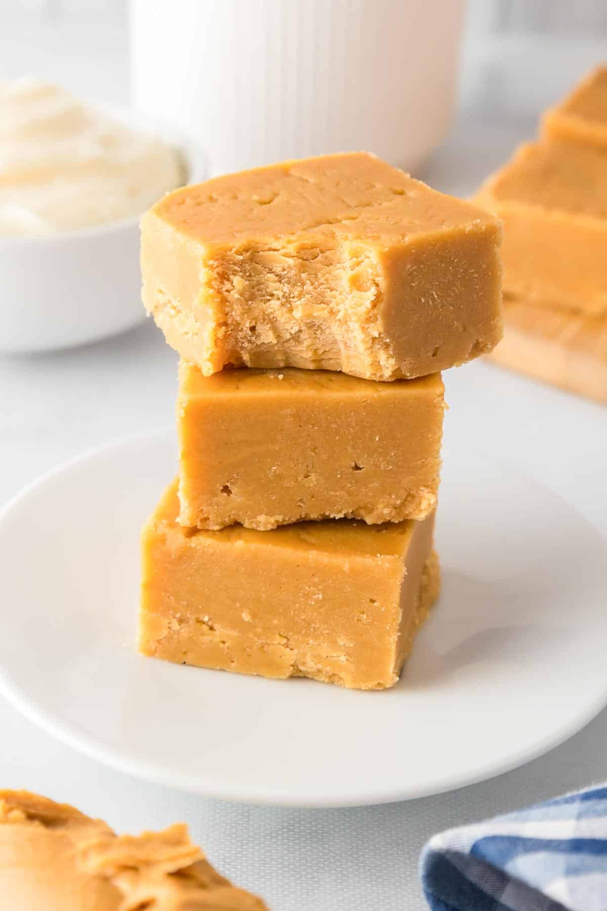 Three pieces of 2 ingredient peanut butter fudge stacked on a white plate on a counter with the top piece missing a bite.