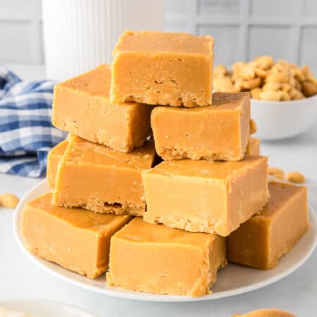 A stack of 2 ingredient peanut butter fudge squares on a plate stacked high from the side on a counter.